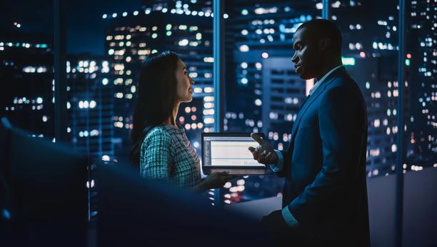 Investment professionals exchanging ideas in front of financial market dashboards