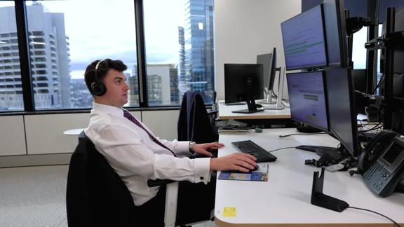Financial professional wearing headphones working on multiple computer monitors in a modern office