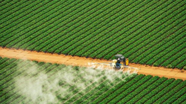 Drone view of a tractor spraying crops between rows of green farmland.
