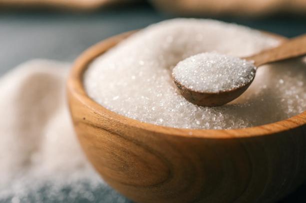 Diferentes tipos de açúcar exibidos sobre uma superfície escura, incluindo açúcar refinado, cristal, mascavo e em cubos.