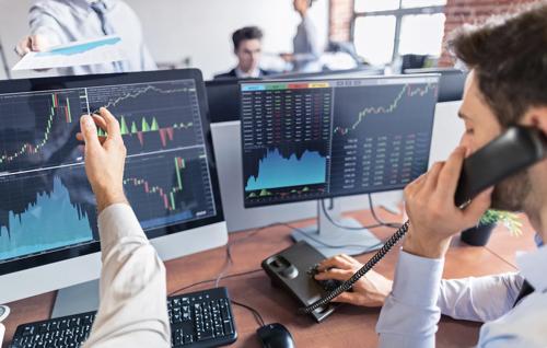 Stock trader analyzing financial charts on multiple monitors while talking on the phone in a busy office