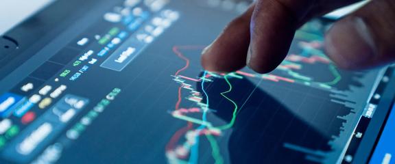 Close-up da mão interagindo com um gráfico de negociação financeira em um tablet com tela sensível ao toque