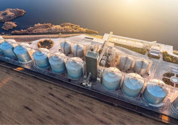 Aerial view of a modern grain storage facility with silos near a body of water and farmland