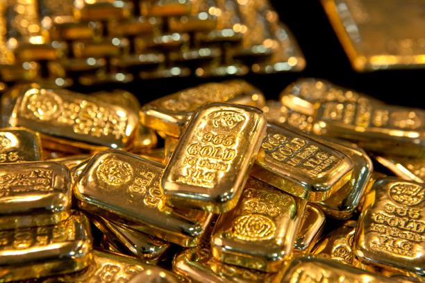 Stack of shiny gold bars arranged closely together, showing detailed engravings on their surfaces.