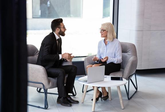 Business professionals having a conversation in a modern office lounge with a laptop on the table.