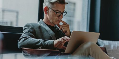 Person wearing glasses and wireless earbuds using a tablet while seated indoors.