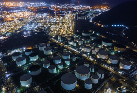 Vista aérea de uma refinaria de petróleo à noite, mostrando tanques de armazenamento e instalações industriais iluminadas por luzes