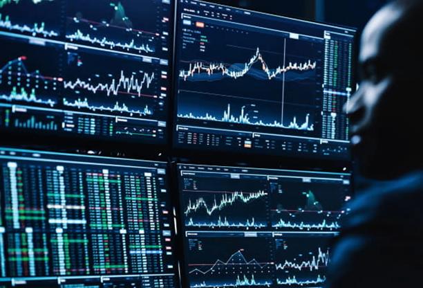 Vários monitores exibindo gráficos financeiros, cotações de ações e dados de negociação em tempo real