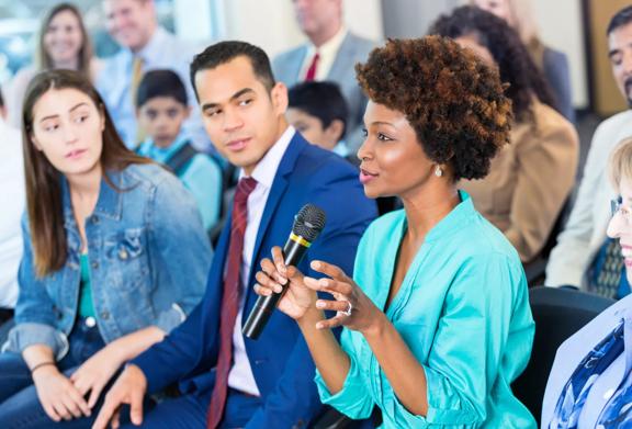 Confident woman holding a microphone and speaking during a community or business event with a diverse audience