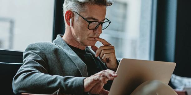 Professional using a laptop and wireless earbuds while reviewing online financial information in a modern office environment. Digital trading and market research concept representing financial analysis, investment planning, and online trading activities.