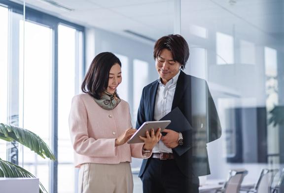 Two business professionals standing in a bright modern office, reviewing information on a digital tablet.