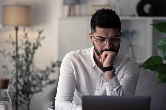 Pessoa trabalhando em casa com notebook sobre mesa, ambiente com plantas e luminária