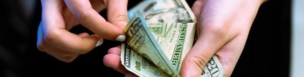 Person handing over cash at a payment counter, symbolizing consumer spending and inflationary pressure on households
