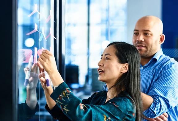 Dois colegas de trabalho fazendo brainstorming e colaborando em um quadro branco com post-its em um escritório moderno