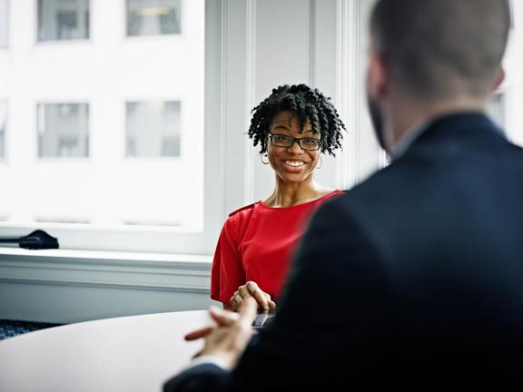 Smiling professional woman in a red blouse having a conversation with a colleague in a bright office