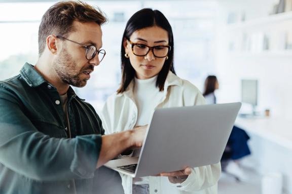 Two business professionals reviewing information together on a laptop in a modern office environment.