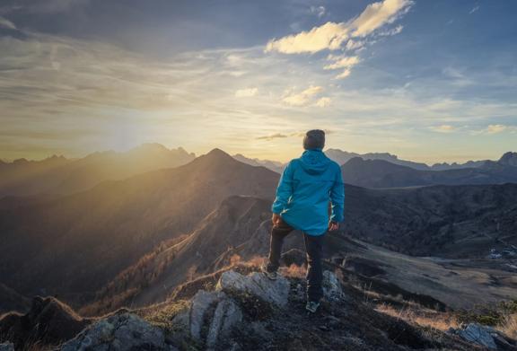 Caminhante em pé no pico da montanha ao nascer do sol, com vista para uma paisagem montanhosa cênica