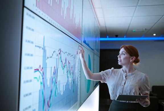 Mulher de negócios analisando gráficos financeiros e visualizações de dados em uma grande tela interativa