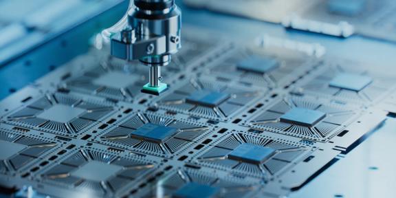 Advanced semiconductor manufacturing process showing microchips on a circuit board being assembled by precision robotic equipment, representing technology innovation, electronics production, and industrial automation.