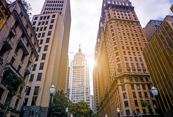 Paisagem urbana do centro de São Paulo com arranha-céus históricos e modernos iluminados pelo sol poente.
