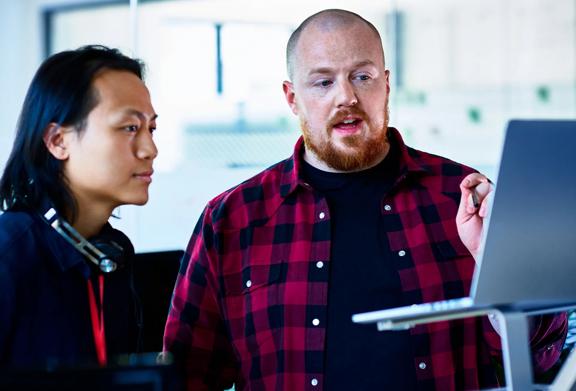 Two male coworkers discussing something on a laptop screen in a modern office setting