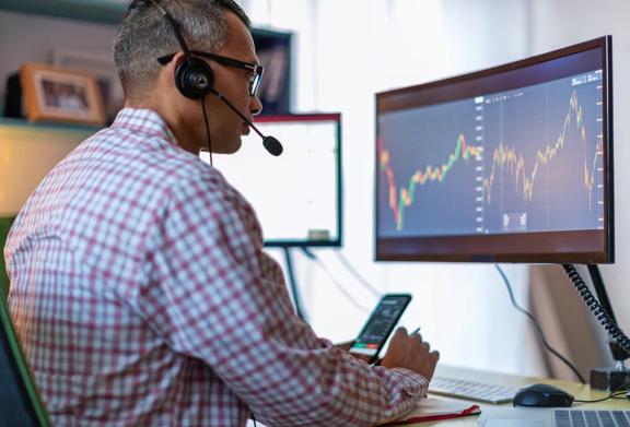 Trader wearing a headset analyzing stock market charts on a monitor while using a smartphone