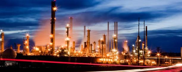 Refinaria industrial à noite com chaminés de fumaça e maquinário iluminados