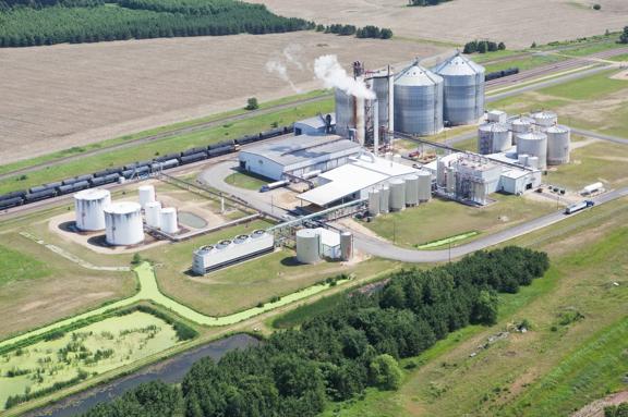 Instalação agroindustrial com silos de armazenamento, tanques e unidade de processamento cercada por áreas agrícolas.