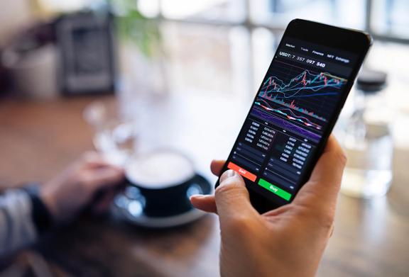 Pessoa usando um aplicativo de negociação de smartphone para monitorar gráficos financeiros e dados de mercado em um café