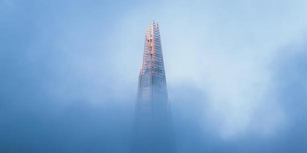 Modern skyscraper rising through low clouds and mist, symbolizing global finance, corporate investment, and financial market infrastructure.