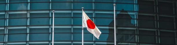 Japanese flag flying in front of glass office building, symbolizing Japan’s economy, governance, and financial markets