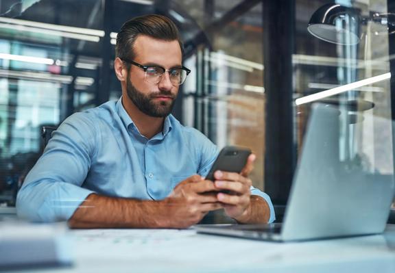 Trader in modern office working on laptop while holding smartphone