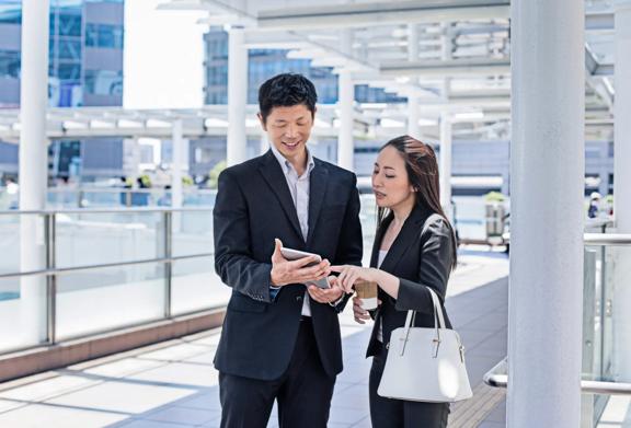 Two business professionals standing outdoors in a modern urban setting, reviewing information on a smartphone.