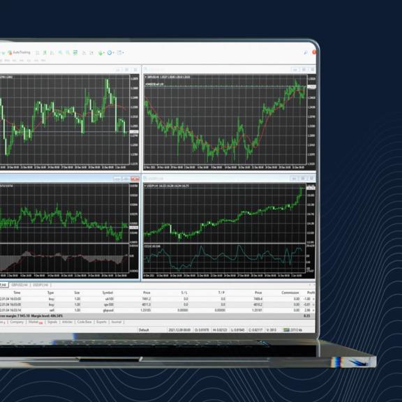 A laptop displaying a trading platform with four market charts showing price movements and technical indicators.