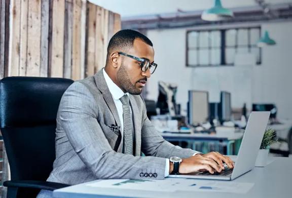 Business professional in a gray suit working intently on a laptop in a modern office environment