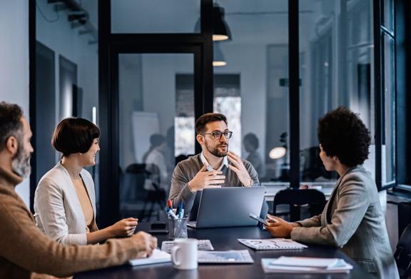 Business team in formal attire engaged in a strategy meeting around a conference table in a modern glass-walled office.