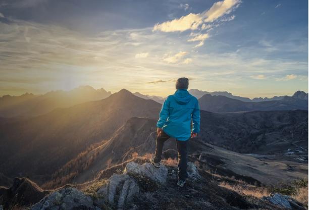 Person standing on a mountain peak during sunset, looking at the vast landscape