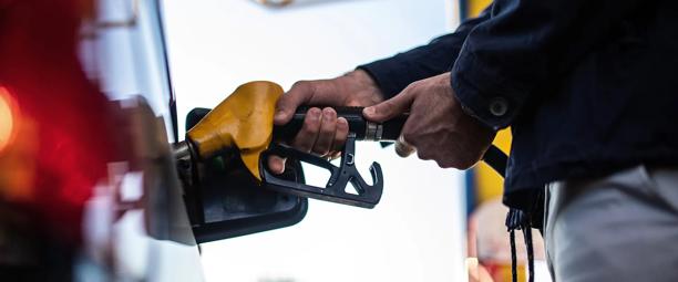 Close-up de uma pessoa abastecendo um carro em um posto de gasolina, segurando o bico da bomba de combustível
