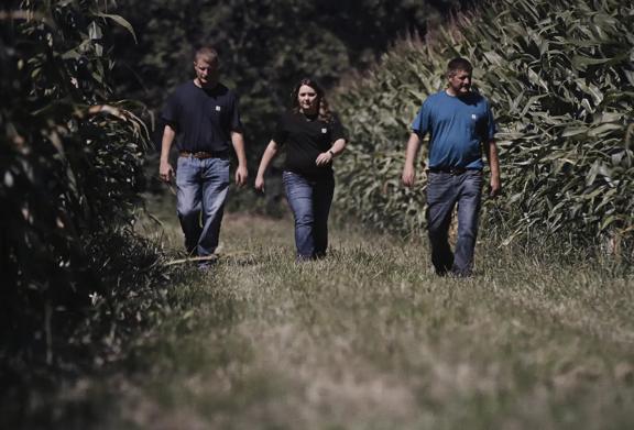 Three agricultural professionals walking through a cornfield during a farm inspection and crop assessment