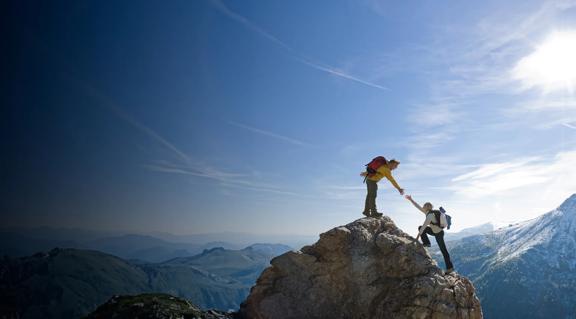 Two hikers helping each other reach the summit of a mountain.