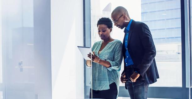 Two business professionals standing in an office discussing information on a digital tablet
