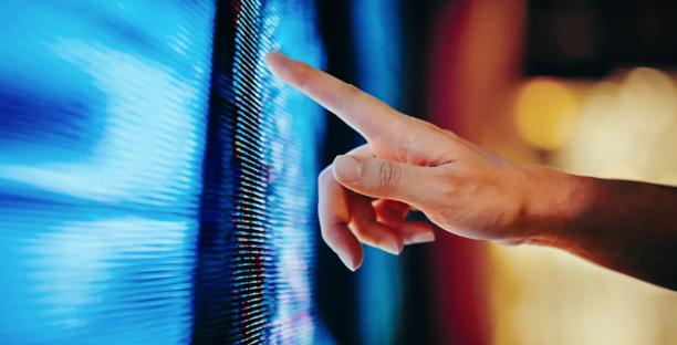 Hand pointing at digital financial data on a large LED screen displaying market trends