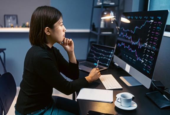 Profissional concentrado analisando gráficos financeiros em um computador de mesa em um escritório doméstico moderno