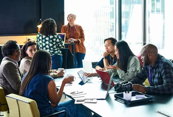 Equipe diversificada de profissionais colaborando em um ambiente de escritório moderno com laptops e notebooks ao redor de uma mesa de conferência.