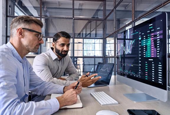 Two men looking at a desktop and laptop screen