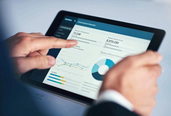 Businessman analyzing performance metrics on a digital dashboard using a tablet, including graphs, pie charts, and KPI data.