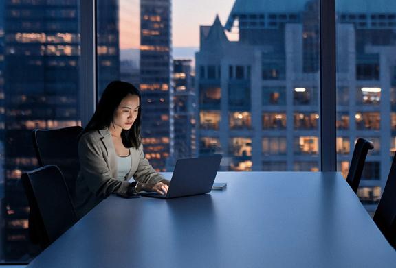 Mulher trabalhando tarde da noite em um escritório com vista para a cidade.