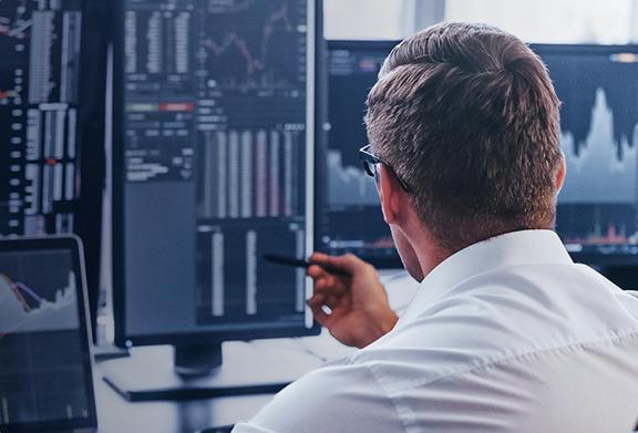 Financial analyst reviewing stock market data on multiple computer screens in an office