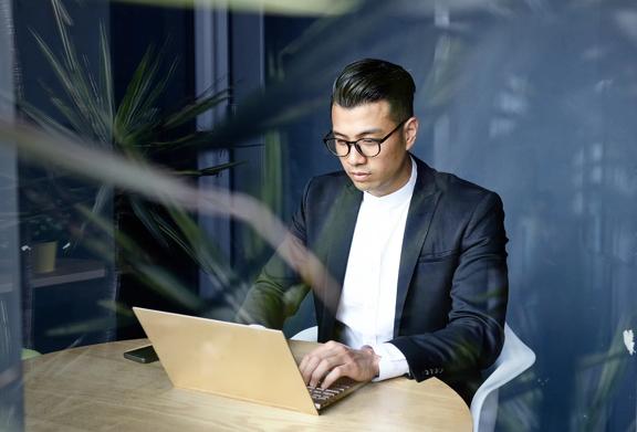 Jovem profissional de terno trabalhando em um laptop em uma mesa redonda de madeira em um escritório moderno
