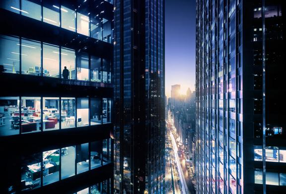 Modern office buildings with illuminated windows overlooking a busy city street at dusk